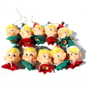 May include: A collection of vintage Christmas elf head ornaments. Each elf has a painted face with blue eyes, yellow hair, and a green or red felt collar and hat. Gold string loops are attached for hanging.
