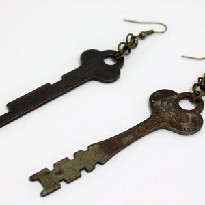 May include: A pair of key-shaped earrings with a bronze finish. The keys are attached to a chain with a hook closure.