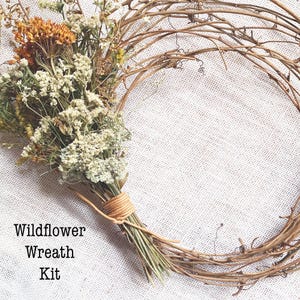 May include: A wildflower wreath kit featuring a circular brown twig frame and a bundle of dried flowers in shades of orange, yellow, and cream, tied together with a light tan cord. The text Wildflower Wreath Kit is printed on the left side.