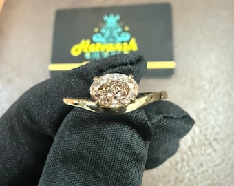 May include: A gold ring featuring a large, oval-shaped, light brown gemstone. The ring's band is a thin, polished gold. The ring is held by a gloved hand, with a business card in the background that has the text "Havanah".