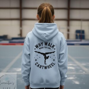 May include: A light blue hoodie with the text "WHY WALK WHEN YOU CAN... CARTWHEEL" and a black graphic of a gymnast doing a cartwheel. The hoodie has a drawstring hood and a kangaroo pocket.