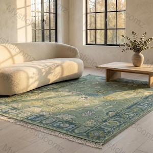 May include: A light green and blue patterned rug with a cream-colored fringe sits on a light wood floor. A curved cream-colored sofa and a wooden coffee table are in the background. The room has large windows.