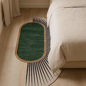 Puede incluir: Una alfombra ovalada verde y beige con un diseño geométrico. La alfombra presenta un centro verde oscuro, un borde beige y un patrón en forma de abanico en negro y beige. La alfombra está colocada cerca de una cama con ropa de cama beige.