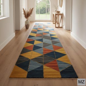 May include: A long runner rug with a geometric design of triangles in yellow, orange, blue, and grey. The rug is placed in a hallway with light wooden flooring and white walls. The rug's pattern is repeated.