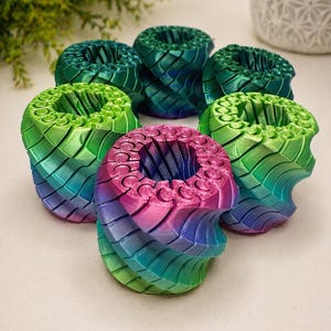 Könnte beinhalten: Sechs farbenfrohe, 3D-gedruckte dekorative Pflanzgefäße. Die Pflanzgefäße sind zylindrisch mit einem strukturierten, geschichteten Design. Die Farben gehen von Grün über Blau bis Rosa. Die Pflanzgefäße sind kreisförmig angeordnet.