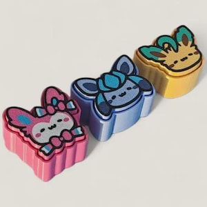 Peut inclure: Trois figurines de personnages de dessins animés en forme de lapin ou de renard. Les figurines ont des bases roses, bleues et jaunes. Chaque figurine a un visage détaillé et est soulignée en noir. Couleurs vives.