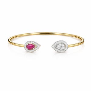 Pode incluir: Uma pulseira dourada com um rubi e um diamante em forma de gota em cada extremidade. As pedras preciosas são rodeadas por um halo de pequenos diamantes. A pulseira é exibida em um fundo branco.