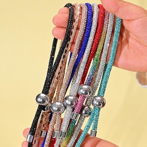 Könnte beinhalten: Eine Sammlung farbenfroher, funkelnder Perlenketten. Die Halsketten sind in verschiedenen Farben erhältlich, darunter Schwarz, Roségold, Silber, Blau, Rot, Grün und Türkis. Jede Halskette hat eine silberne Metallperle und einen silbernen Metallverschluss.