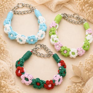 May include: Three macrame dog collars with flower designs. One collar is blue and white, another is green and pink, and the third is green, pink, and red. Each collar has a silver chain.