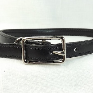 May include: A black leather belt with a silver buckle. The belt is about 1 inch wide and has a simple design.