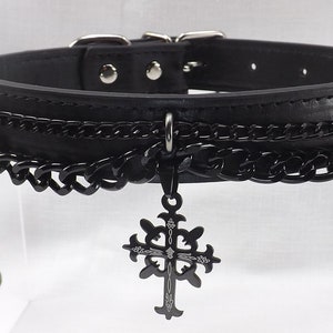 May include: Black leather choker with multiple black chains and a dangling silver cross pendant. The chains have iridescent blue beads at the ends.