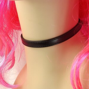 May include: A black leather choker necklace on a mannequin with pink hair.