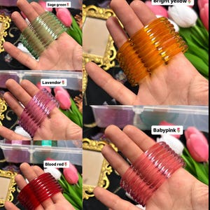 Könnte beinhalten: Eine Sammlung farbenfroher, durchscheinender Armreifen in Salbeigrün, leuchtendem Gelb, Lavendel, Blutrot und Babyrosa. Jeder Armreif wird auf einer Hand präsentiert, um die verschiedenen Farben und Texturen zu zeigen. Das Bild enthält Textbeschriftungen für jede Farbe.