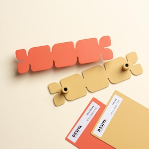 Puede incluir: Dos objetos decorativos rectangulares abstractos, uno coral y otro beige, cada uno con un diseño floral en los extremos. Dos muestras de color debajo, etiquetadas como "Morelowy" y "Honey" con la marca "Desiva".