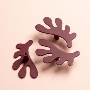 K&ouml;nnte beinhalten: Drei weinrote Schrankgriffe mit einem abstrakten, organischen Design. Die Griffe haben eine matte Oberfl&auml;che und eine einzigartige, verzweigte Form, die an Korallen oder Pflanzen erinnert. Die Griffe sind aus Metall gefertigt und f&uuml;r M&ouml;bel bestimmt.