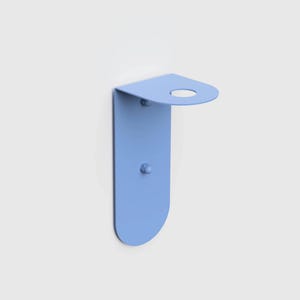 Op de afbeelding: Een lichtblauwe metalen wandhouder met een verticale rechthoekige plaat met afgeronde onderranden en een haakse bovenplank met een cirkelvormige uitsparing. De houder is aan de muur bevestigd met twee zichtbare metalen bevestigingsmiddelen.