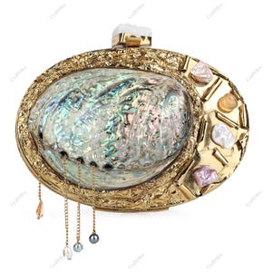 May include: An oval-shaped, gold-toned clutch with an iridescent abalone shell center. The clutch features decorative gold trim, gemstone accents, and dangling chains with beads. A white crystal adorns the clasp.
