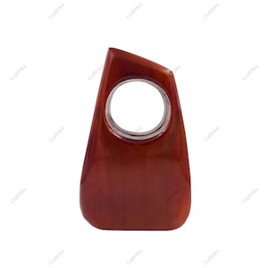 Puede incluir: Un tirador de puerta de madera, de color marrón rojizo. El tirador tiene una forma lisa y curvada con una abertura circular en el centro. Probablemente para un armario o un cajón.