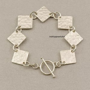 Puede incluir: Una pulsera de plata con eslabones cuadrados y en forma de diamante martillados. La pulsera tiene un cierre de palanca. El texto "IndriyajewelsArt" es visible en la pulsera.