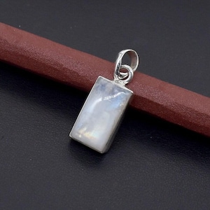 May include: A rectangular pendant with a silver bail and a rectangular, iridescent, light blue and white stone. The pendant is set in a silver bezel and is displayed against a dark background.