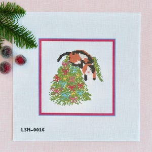 May include: Cross-stitch design featuring a calico cat perched atop a decorated Christmas tree. The tree is adorned with colorful ornaments and bows. The design is framed with a pink and blue border, and the text "LSN-0016" is at the bottom.