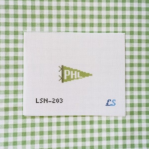 May include: A white needlepoint canvas featuring a centered green pennant design with the letters PHL in white. The text LSM-203 is printed in black on the lower left, and the blue letters LS are printed on the lower right of the canvas.