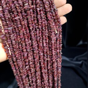 May include: Strands of small, irregularly shaped, deep red gemstones. The beads are strung together, creating a textured and visually appealing display. The gemstones have a natural, organic appearance.