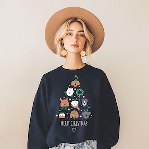 Op de afbeelding: Marineblauw sweatshirt met een kerstboomontwerp gemaakt van verschillende hondenrassen. De woorden "MERRY CHRISTMAS" staan onder de boom, met een hartsymbool. Het sweatshirt is een crew neck stijl.
