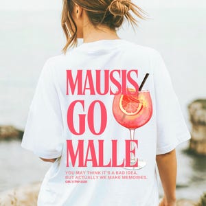May include: White t-shirt with the words "MAUSIS GO MALLE" in pink, along with a watercolor illustration of a cocktail. The text "YOU MAY THINK IT'S A BAD IDEA, BUT ACTUALLY WE MAKE MEMORIES. GIRL'S TRIP 2026" is also printed on the shirt.