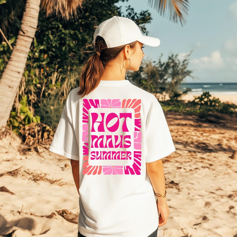 Puede incluir: Camiseta blanca con un gr&aacute;fico rosa y fucsia que dice "HOT MINUS SUMMER". El dise&ntilde;o est&aacute; enmarcado con un patr&oacute;n floral. La camiseta se usa en una playa con palmeras y el oc&eacute;ano de fondo.