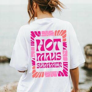 Puede incluir: Camiseta blanca con un vibrante dise&ntilde;o floral rosa y naranja. La camiseta presenta las palabras "HOT MINUS SUMMER" en una fuente retro. El dise&ntilde;o est&aacute; centrado en la parte posterior de la camiseta, creando una declaraci&oacute;n audaz.