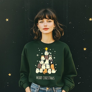 Op de afbeelding: Een donkergroene sweatshirt met een kerstboomontwerp van cartoonkatten. De katten hebben verschillende kleuren en patronen, bekroond met een gele ster. De woorden "MERRY CHRISTMAS" staan eronder.