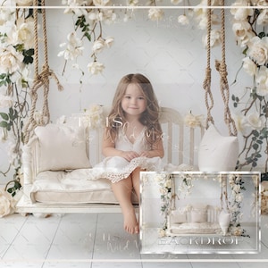 Puede incluir: Una niña pequeña sentada en un columpio blanco con un fondo floral blanco. El columpio está decorado con almohadas blancas y la niña lleva un vestido blanco con encaje.