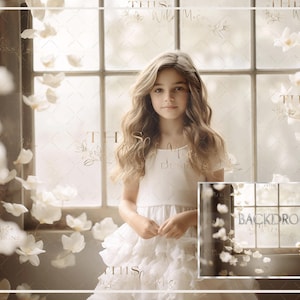 May include: A young girl in a white dress stands in front of a window with white flower petals falling around her. The window is framed in white and has a backdrop of white flower petals.