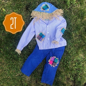 May include: A blue and white striped shirt with a straw hat and blue pants. The shirt has patches of fabric on the shoulders and elbows. The pants have a patch of fabric on one knee. The outfit is labeled "2T".