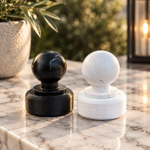 May include: Two circular stone objects, one black and one white, each featuring a spherical top piece resting on a cylindrical base. Both items display natural veining patterns characteristic of marble, with smooth, polished surfaces.