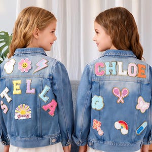 May include: Two light blue denim jackets with colorful patches. One jacket has the name "STELLA" and the other has "CHLOE" on the back. Both jackets feature various patches, including a flower, lightning bolt, and a rainbow.