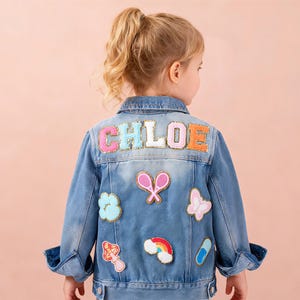 May include: A light blue denim jacket with the name "CHLOE" in colourful embroidered letters on the back. The jacket is decorated with patches of a tennis racket, butterfly, mushroom, rainbow, cloud, and a capsule.