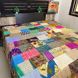 May include: A patchwork quilt in a variety of colors, including blue, pink, green, and yellow, covers a bed. The quilt is made of many different fabric squares sewn together. The headboard is black with silver accents and small green decorative trees.