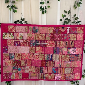 May include: A vibrant pink patchwork textile with a rectangular shape. The textile is composed of numerous fabric squares in varying shades of pink, adorned with gold accents and intricate patterns. The text "Desi company" is visible on the textile.