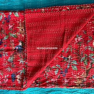 May include: Red quilted textile with a floral and bird pattern. The design features various birds, flowers, and foliage in shades of blue, green, and pink. The textile is stitched with white thread and has the text "NEWINDIAFASHION".