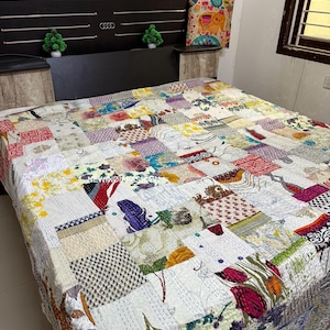 Op de afbeelding: Een patchworkquilt met een verscheidenheid aan kleurrijke stoffen vierkanten. De quilt heeft bloemen- en geometrische patronen in tinten rood, blauw, groen en geel. Het bed is opgemaakt met de quilt en een kussen met een olifantenontwerp.