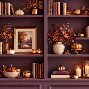 Puede incluir: Una estantería empotrada de color morado oscuro con decoración otoñal que incluye calabazas naranjas y blancas, follaje seco en jarrones, velas en portavelas y un cuadro de un paisaje forestal, todo dispuesto entre filas de libros.