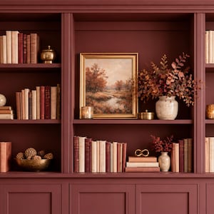 May include: A large, built-in dark red bookshelf featuring three vertical sections filled with rows of books, decorative vases, potted plants, a framed landscape painting, and small metallic bowls arranged on multiple shelves.