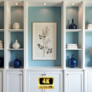 Op de afbeelding: Een ingebouwde witte kast met planken, blauwe accentmuren en diverse decoratieve items. De planken tonen stapels boeken, witte en marineblauwe vazen en een ingelijste botanische print. De afbeelding bevat ook een 4K Ultra HD-logo.