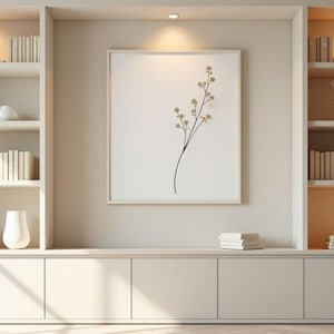 May include: A built-in, neutral-toned bookshelf unit with multiple shelves. The shelves display stacks of books, decorative vases, and small ornamental trees. A framed botanical print hangs in the centre, and the unit is illuminated by recessed lighting.