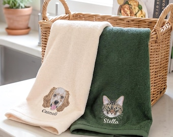 May include: Two embroidered kitchen towels. One is cream-colored with a dog face and the name "Cannoli." The other is dark green with a cat face and the name "Stella." Both towels are folded and placed on a countertop near a sink.