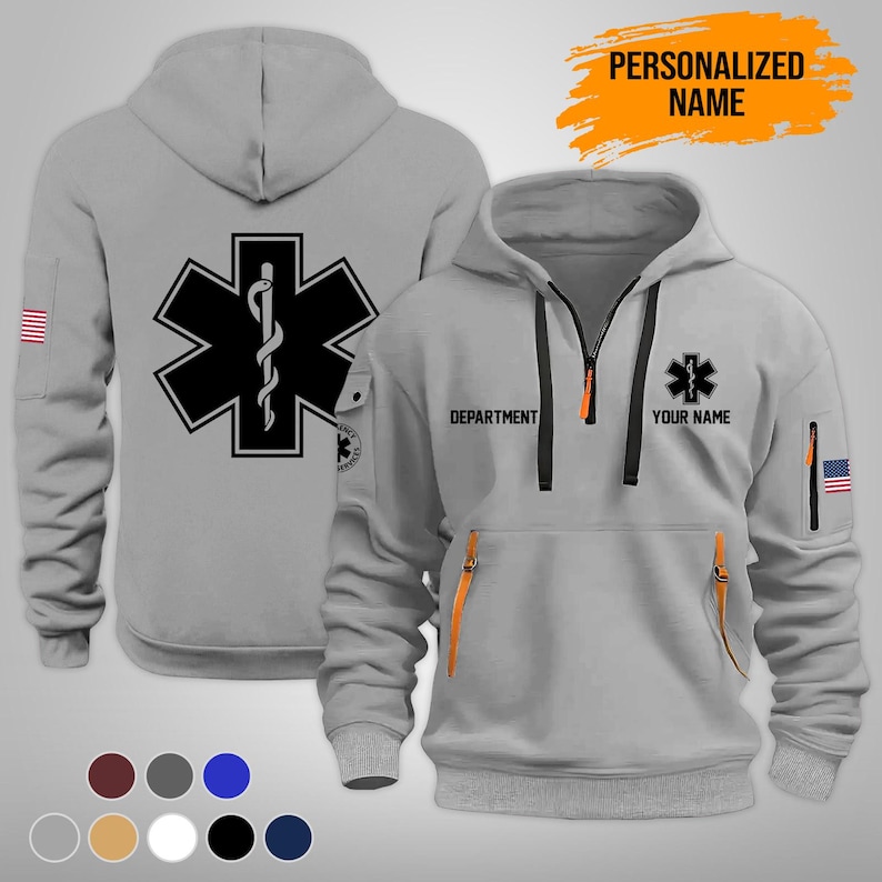 Puede incluir: Una sudadera con capucha gris claro con un s&iacute;mbolo m&eacute;dico negro en la parte delantera y trasera. La parte delantera presenta una cremallera, bolsillos con detalles en naranja y el texto "DEPARTMENT" y "YOUR NAME". Un parche de la bandera estadounidense est&aacute; en la manga.