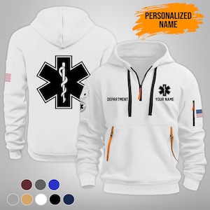 Puede incluir: Sudadera con capucha blanca con un emblema negro y blanco de la Estrella de la Vida en la parte delantera y trasera. Cuenta con cremallera, detalles en naranja y el texto "DEPARTMENT" y "YOUR NAME". Incluye un parche de la bandera estadounidense en la manga. Tambi&eacute;n se ve el texto "PERSONALIZED NAME".