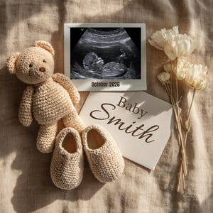 Könnte beinhalten: Ein beigefarbener gehäkelter Teddybär, Babyschuhe und ein Ultraschallbild mit dem Text "Oktober 2026" sind auf einer neutral getönten Oberfläche angeordnet. Eine Karte mit dem Text "Baby Smith" ist ebenfalls vorhanden, zusammen mit weißen Blumen.